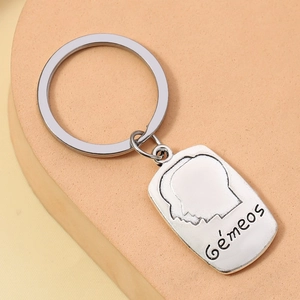 Silver Gemini zodiac keychain with embossed Gémeos tag on orange geometric display