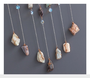 Detail of colorful raw stones wrapped in copper wire with blue crystal beads on silver chains