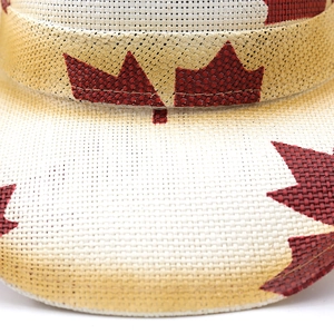 Macro view of woven straw hat featuring detailed red maple leaf print on beige fabric