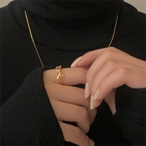 Close-up of golden ribbon bow ring and matching necklace on a black sweater