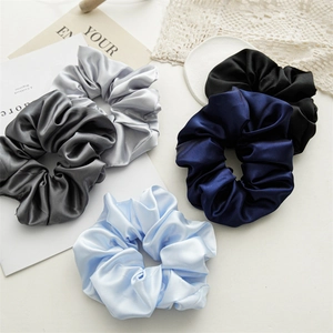 Close-up of five satin scrunchies in assorted colors with a glossy texture and soft folds