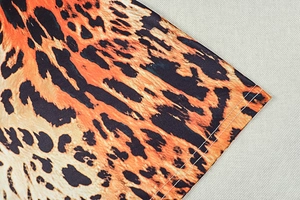 Detail of leopard print fabric showing orange and black pattern with double-stitch hem