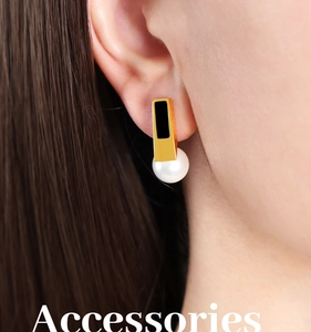 Close-up of gold rectangular earrings with black inlay and round white pearl on ear
