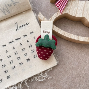 Detail view of a red fabric strawberry hair scrunchie with green leaves on a table
