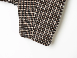 Detailed close-up showing the plaid tweed fabric texture and sleeve stitching of the jacket