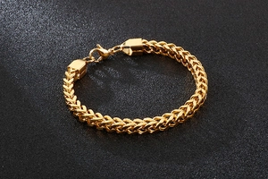 Detailed close-up of golden Franco chain bracelet with lobster clasp on black background