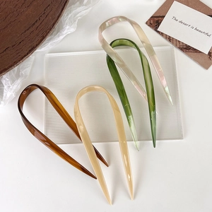 U-shaped hair pins in brown, beige, and green displayed on a soft aesthetic background