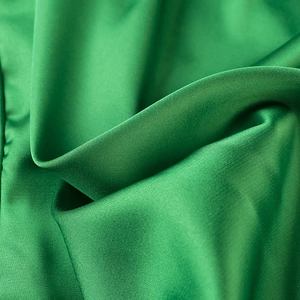 Detailed close-up of smooth green satin fabric showing glossy texture and natural folds