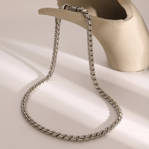 Detail of silver stainless steel curb chain necklace draped over a white ceramic display
