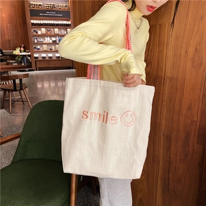Close-up of smile embroidery and wave-pattern woven strap on an off-white canvas tote bag
