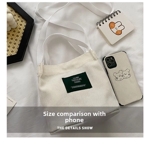 Flat lay of a beige mini canvas bucket bag with green woven label and shoulder strap