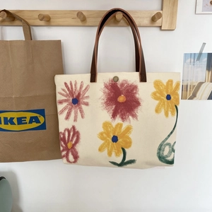 Detail of canvas tote bag featuring artistic floral prints and brown leather handles