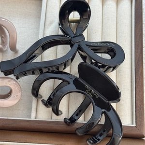 Glossy bow hair claws in black and beige with gold lettering in a velvet tray