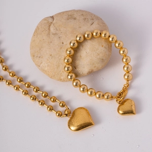 Golden bead necklace and bracelet set with chunky heart pendants on a natural stone background