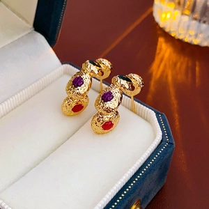Detailed close-up of vintage gold earrings with red and purple gems in a luxury velvet box