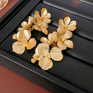 Détail de boucles d'oreilles fleur dorée sur boîte en cuir noir avec pompon métallique