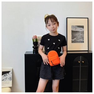 Close-up of orange nylon mini crossbody bag with zipper detail on child model