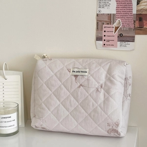 Close-up of a quilted makeup bag in light lavender with animal patterns and woven label