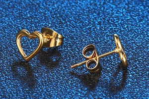 Macro detail of gold hollow heart stud earrings featuring a polished finish on blue background