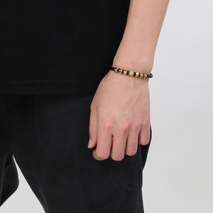 Close-up of men's black braided leather bracelet with golden metallic geometric beads