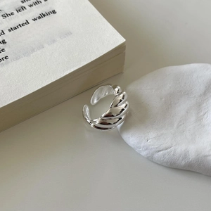 Detailed close-up of a silver twisted croissant ring on a white minimalist stone base