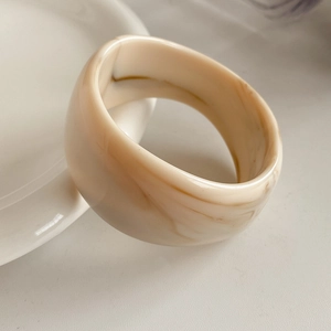 Macro detail of wide cream marble resin ring with smooth polished geometric surface