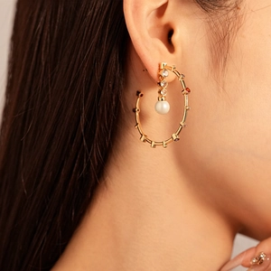 Close-up of golden bamboo hoop earring with white pearl and multicolored rhinestones