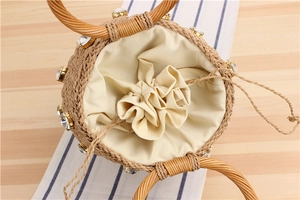Detailed close-up of woven straw cylinder bag with crystal trim and drawstring lining