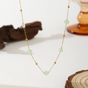 Detail of gold necklace featuring translucent green flower charms and beads on white background