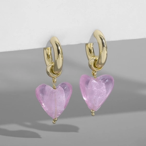 Détail de créoles dorées avec pendentifs cœur en verre rose translucide sur un support