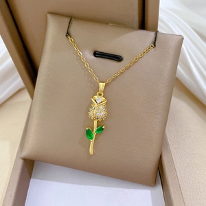 Macro detail of gold rose pendant with sparkling crystals and green gem leaves