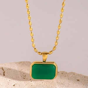 Detail of a geometric gold stainless steel necklace with green tiger eye stone on a stone