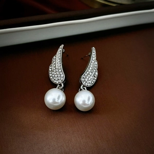 Macro detail of silver angel wing earrings with sparkling rhinestones and a white pearl