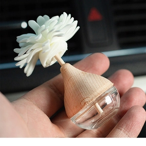 Close-up of a glass reed diffuser bottle with a wooden lid and white flower reed in hand