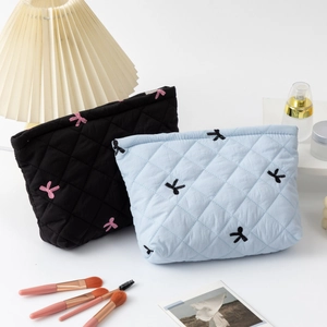 Quilted bow embroidery cosmetic bags in black and blue shown with makeup accessories