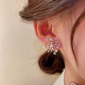 Close-up of elegant gold firework stud earrings with crystals and pearls worn by a model