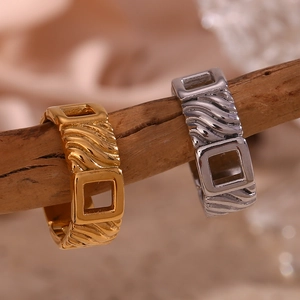 Detailed view of gold and silver square hollow rings with wave textures on a branch