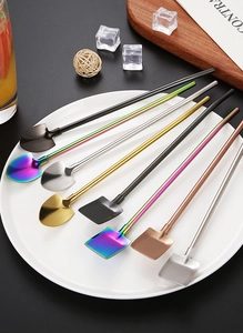 Various colorful stainless steel spade-shaped straw spoons arranged on a white ceramic plate