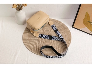 Close-up of beige crossbody camera bag with black and white printed wide strap on a woven mat