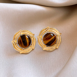 Makroaufnahme von Vintage Goldohrringen mit Tigerauge auf elegantem Seidenstoff