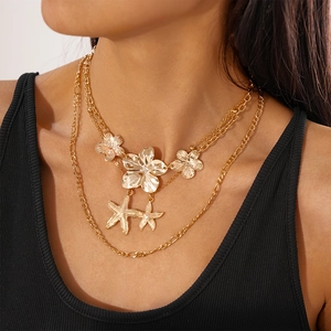 Close-up of golden layered necklace with metallic flowers and starfish charms on a model