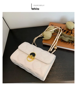 Detail of white quilted chain bag with gold rotary lock on a textured background