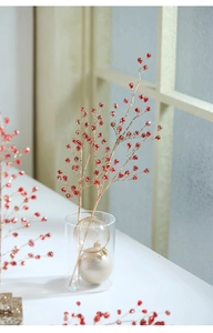 Close-up of festive red artificial berry branches with gold stems in a clear glass vase