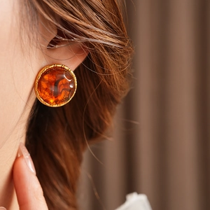 Close-up of model wearing amber resin round earrings with gold gear-shaped borders
