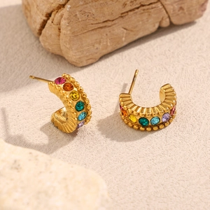 Detail of 18K gold C-shaped earrings with colorful zircon stones on textured stone