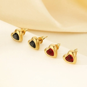 Close-up of golden heart earrings with black and red gems on soft beige fabric