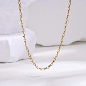 Detail shot of golden stainless steel box chain necklace on white marble rock