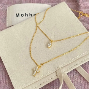 Close-up of gold S925 silver double-layered cross and marquise stone necklaces on suede pouch