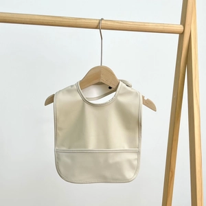 Close-up of beige waterproof baby bib with food catcher pocket on wooden hanger
