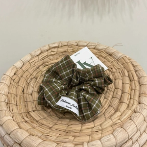 Close-up of forest green plaid scrunchie with white brand label on woven background